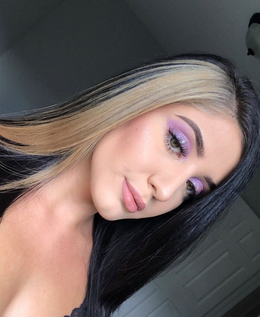 “Close-up of a woman with sleek black hair featuring a bold blonde streak, wearing purple eye makeup and a natural lip color.”