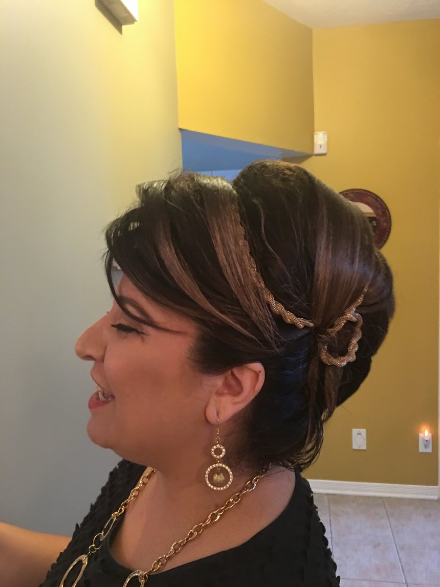 “Elegant updo hairstyle with braided details and highlights, worn by a woman dressed in gold jewelry, captured in a warmly lit setting.”