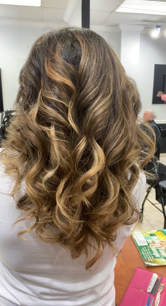 “Long, golden brown hair styled in soft, defined curls, showcasing a vibrant and voluminous finish, photographed in a salon.”