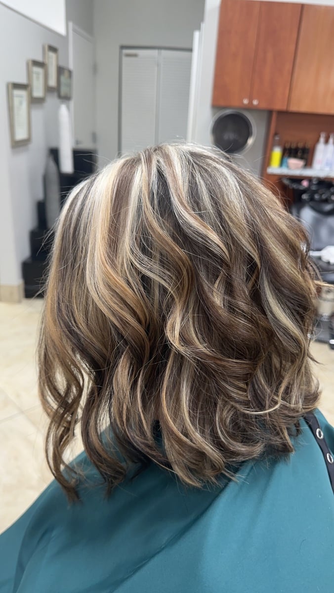 “Shoulder-length wavy hair with blonde and caramel highlights, styled with volume and texture, captured in a salon setting.”