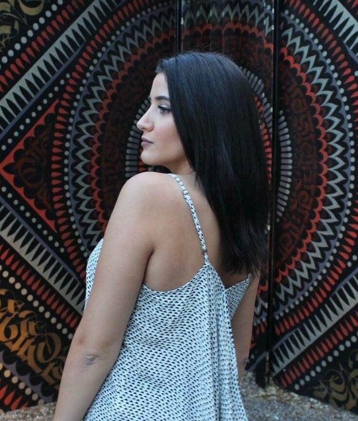 “Woman with sleek, straight dark hair wearing a patterned dress, posing outdoors against a decorative patterned background.”